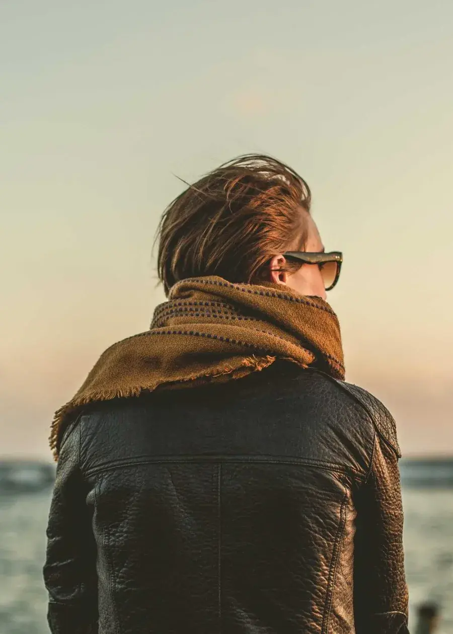 Placeholder portrait: a figure in a leather jacket seen from behind, facing the sea